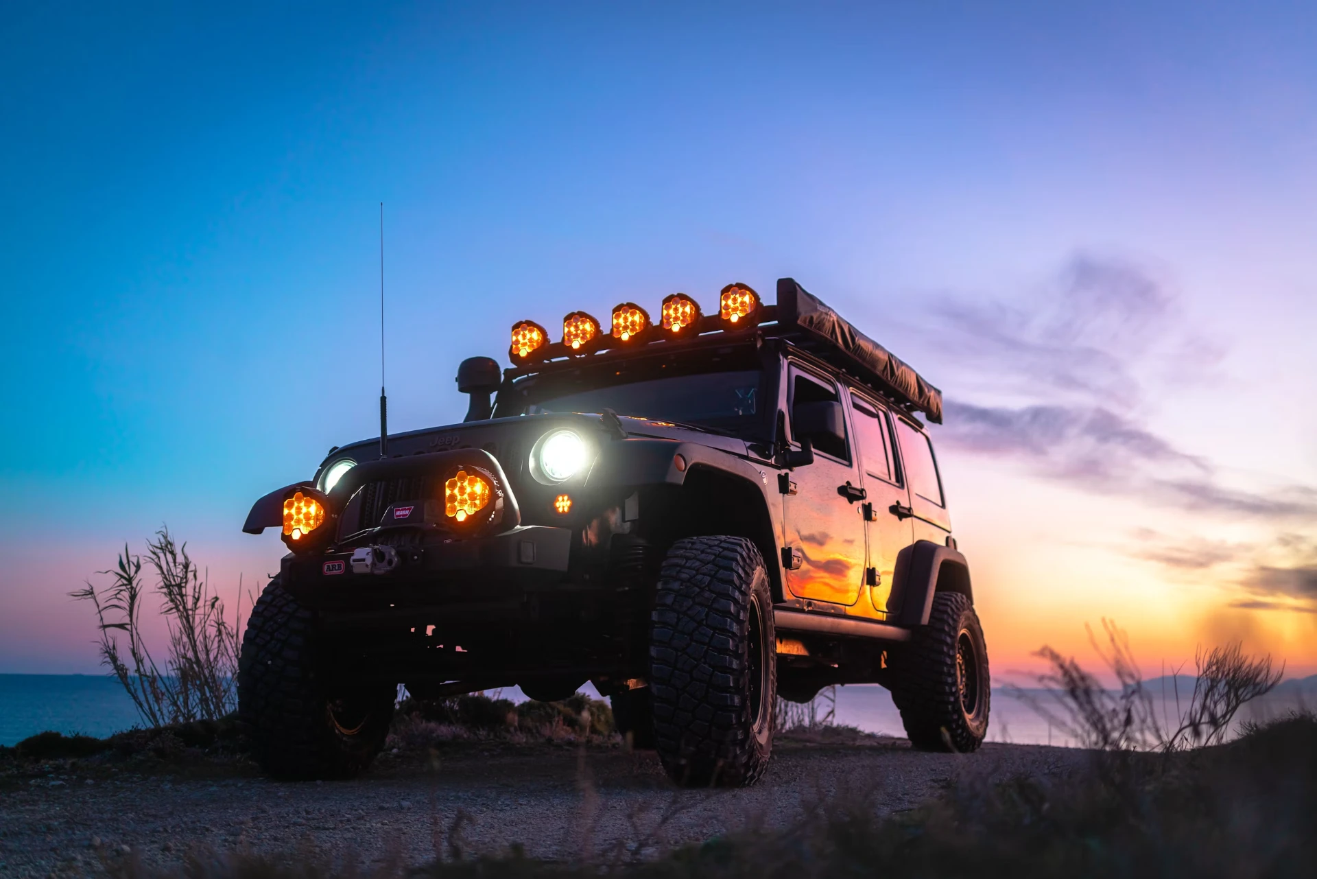 Lifted Jeep Wrangler with light bar at sunset by the coast